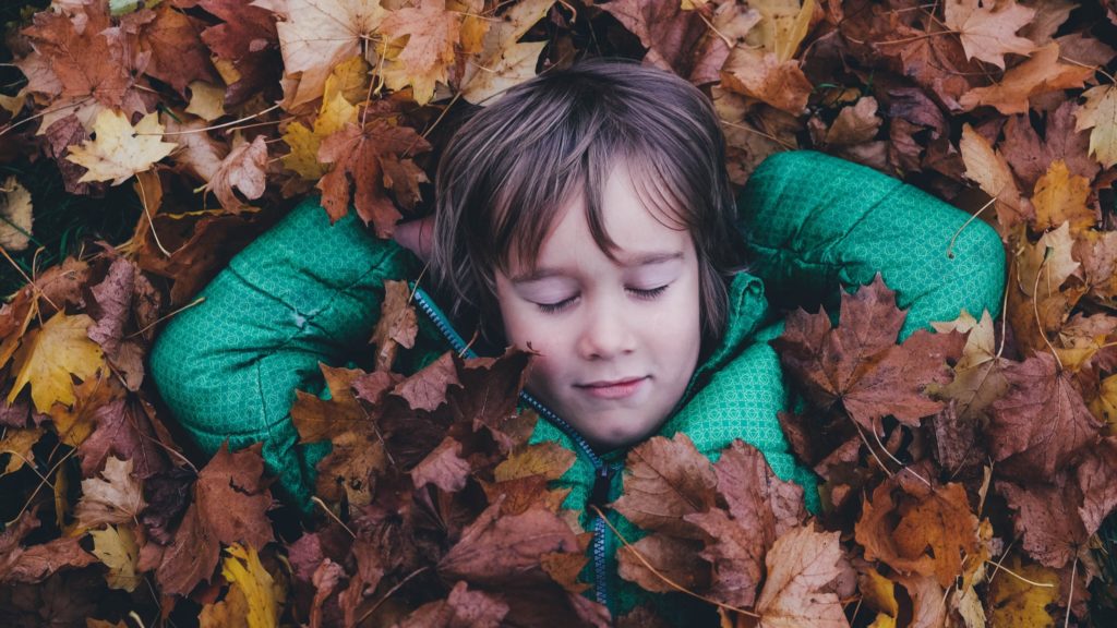 Ein Kind schläft im Herbstlaub.